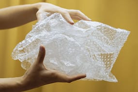 pexels-photo-7829815 Close-up of hands holding and crumpling bubble wrap against a yellow backdrop indoors.